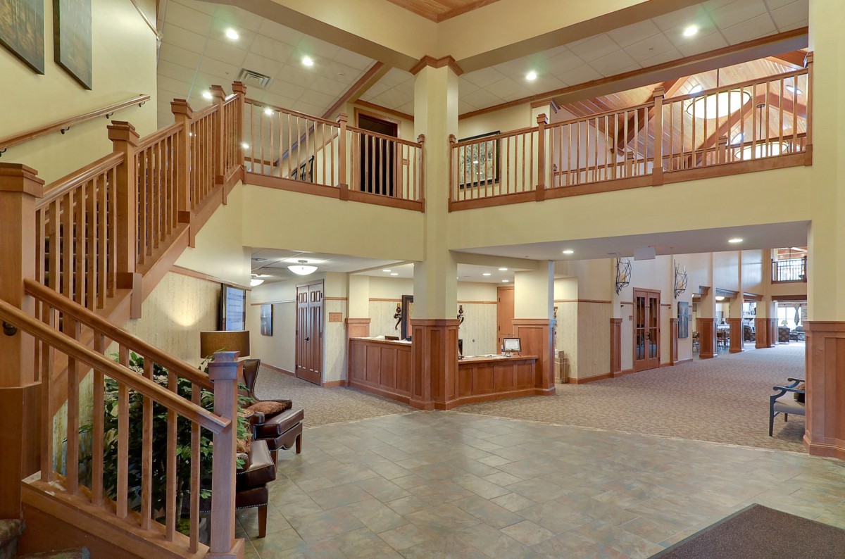 A spacious hotel lobby with a reception desk, staircase, and wooden accents.
