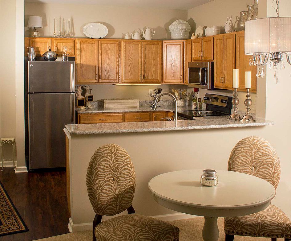 A modern apartment kitchen with wood cabinets and stainless steel appliances, featuring a cozy dining area.
