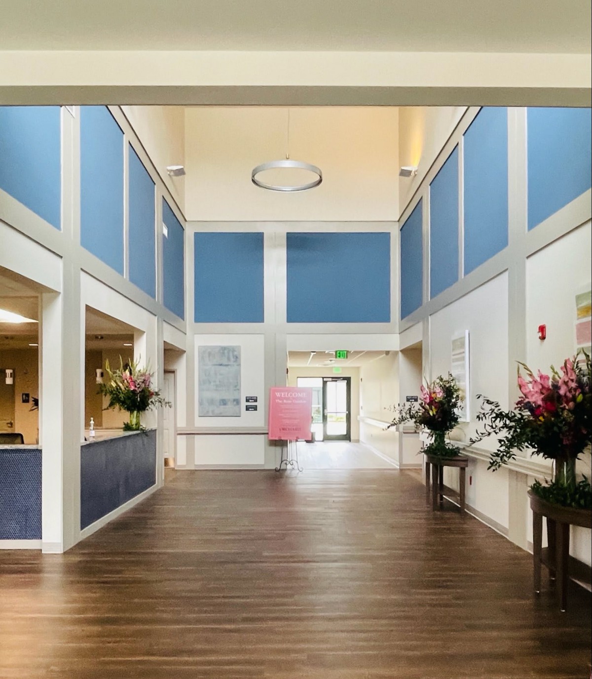 A spacious lobby with blue accents, wooden flooring, and decorative flower arrangements.