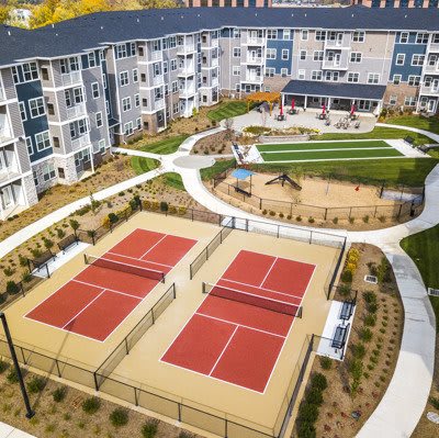 Aerial view of a modern apartment complex with tennis courts and landscaped outdoor areas.