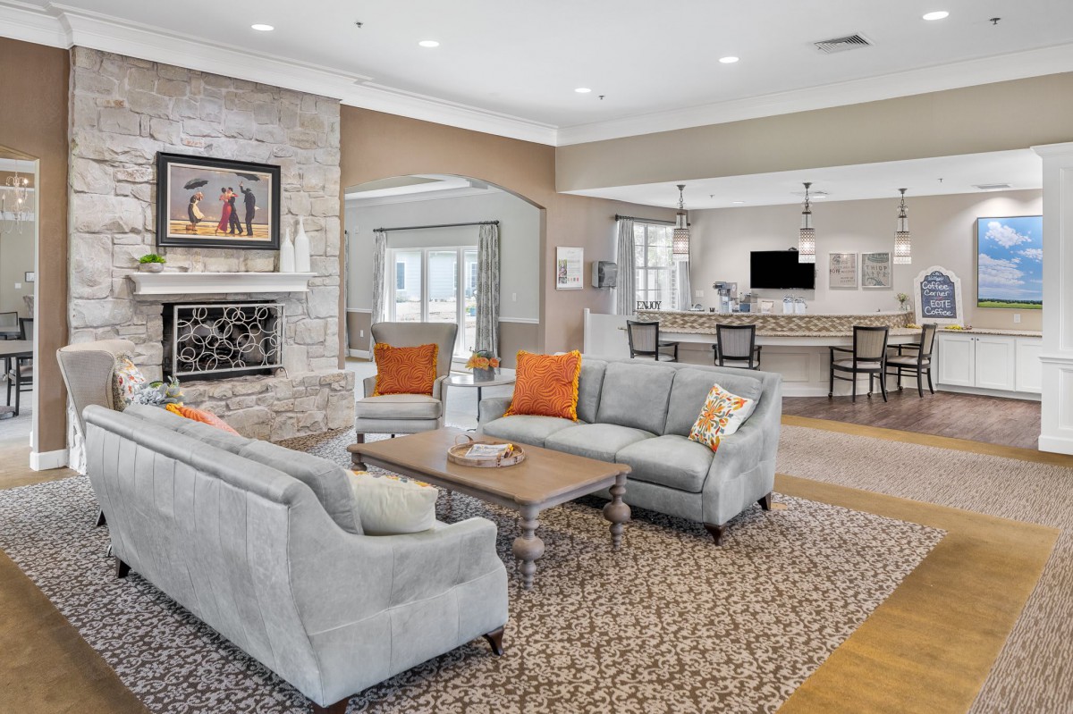 A modern living room with an open concept design, featuring comfortable sofas, a coffee table, and a fireplace, leading to a kitchen area.