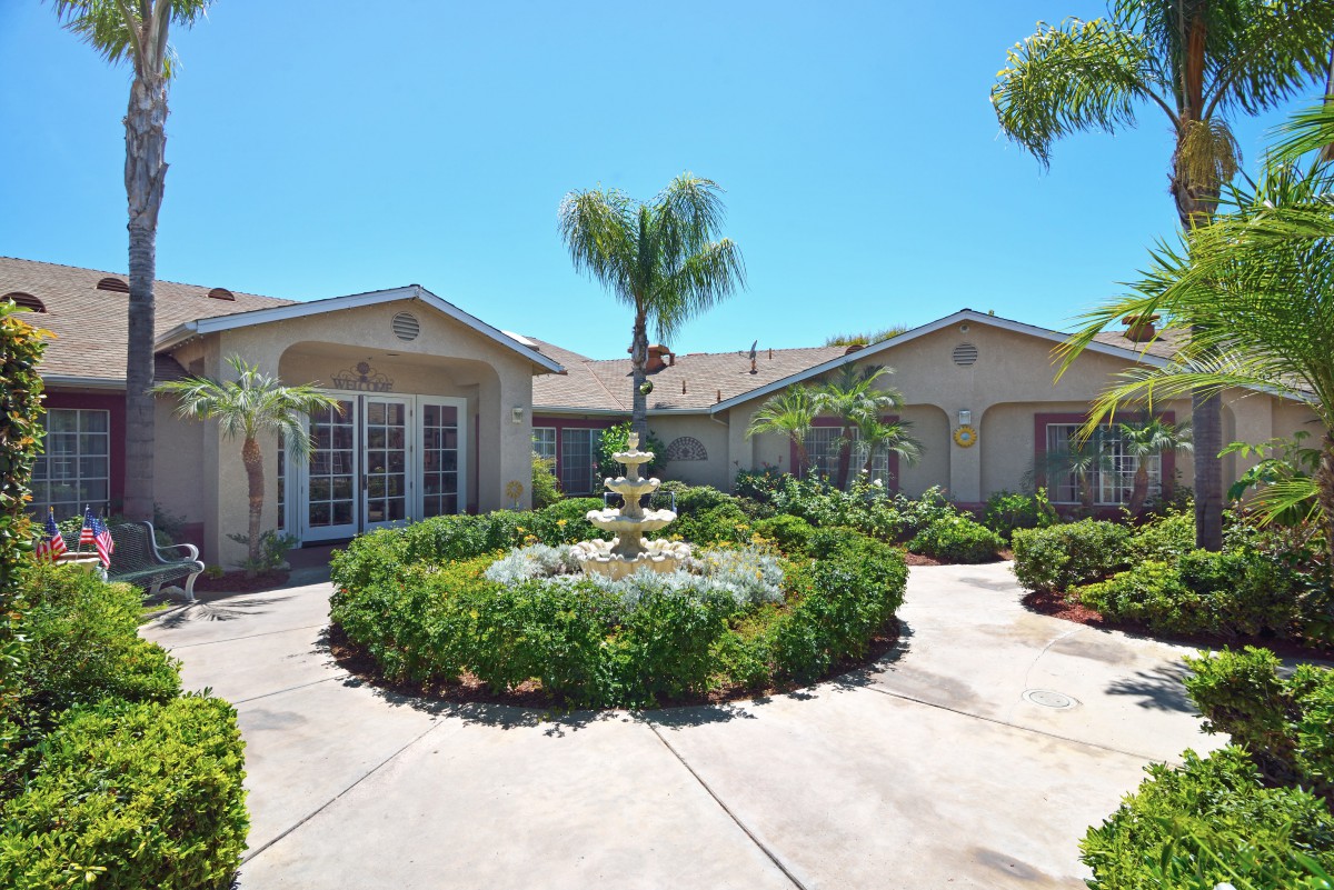 A beautiful house with a round driveway and central fountain surrounded by lush landscaping.