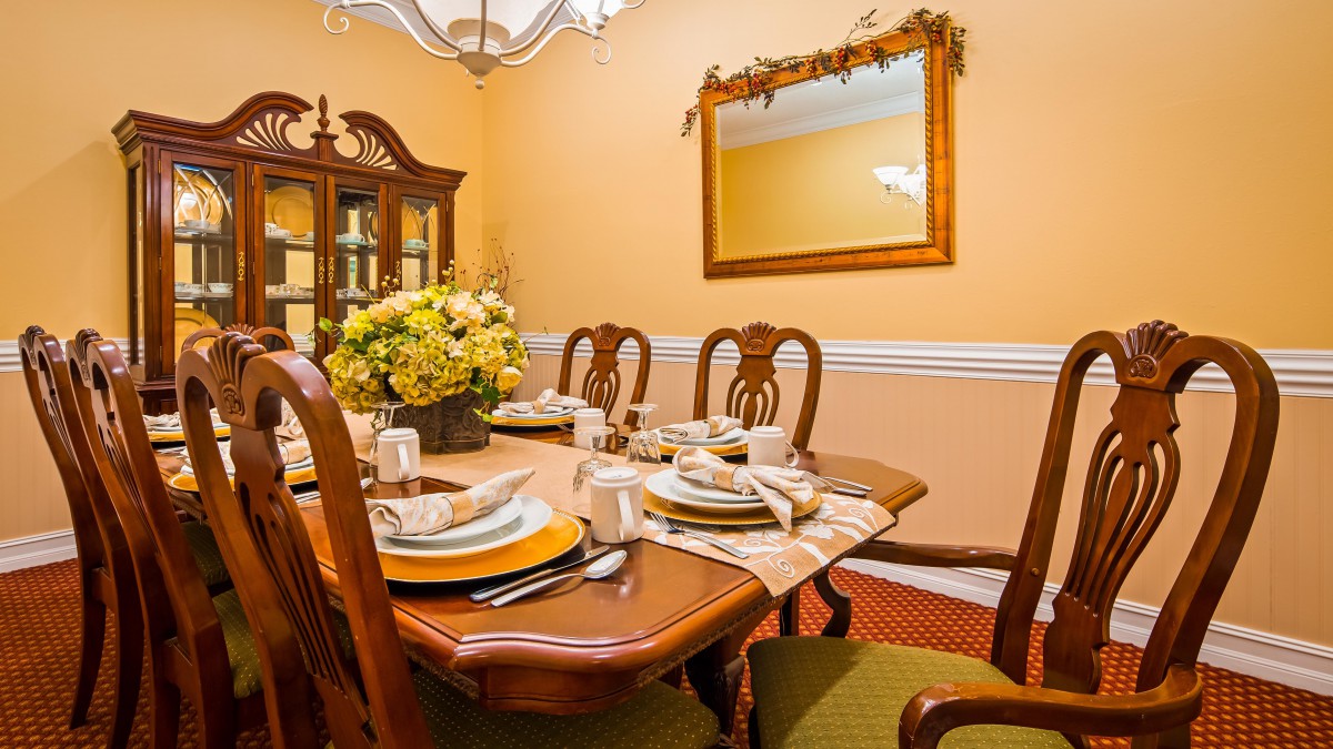 A warmly decorated dining room with a table set for a meal, featuring elegant wooden furniture and a floral centerpiece.