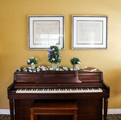A beautifully arranged piano with floral decor and framed sheet music on the wall.