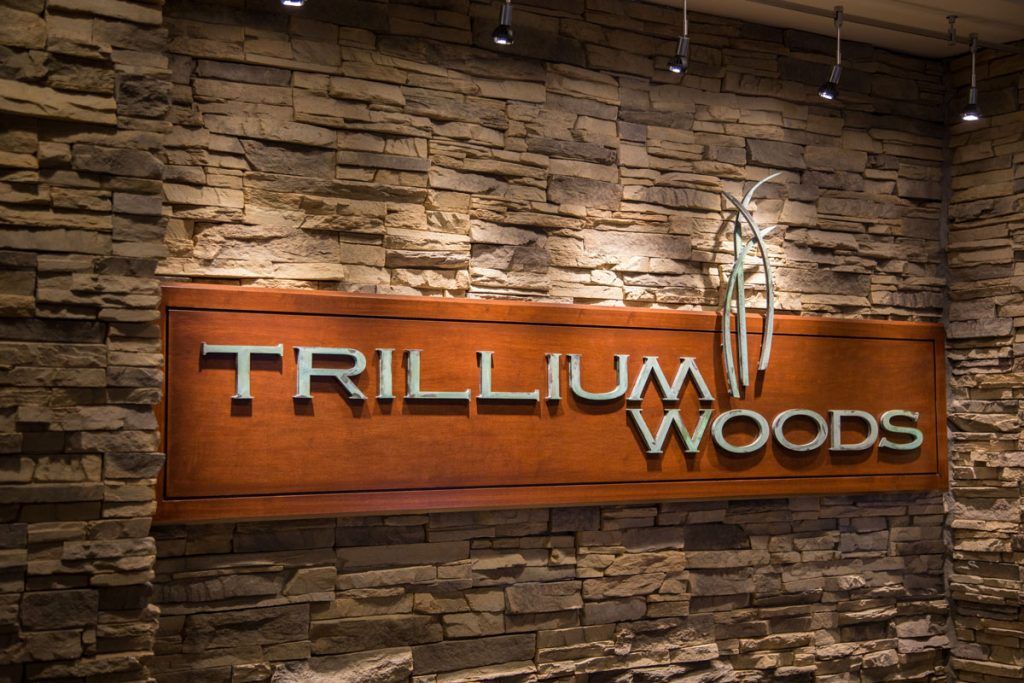Illuminated Trillium Wood sign mounted on a stone wall.