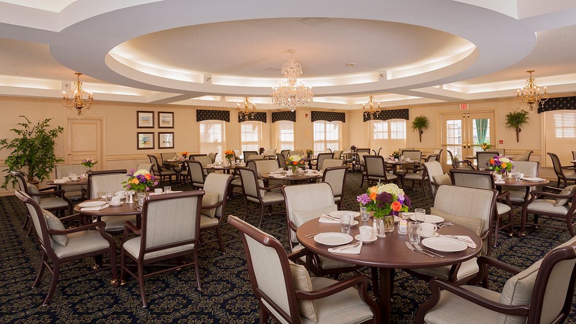 An elegant dining room with neatly arranged tables and chairs, decorated with flowers and chandeliers.