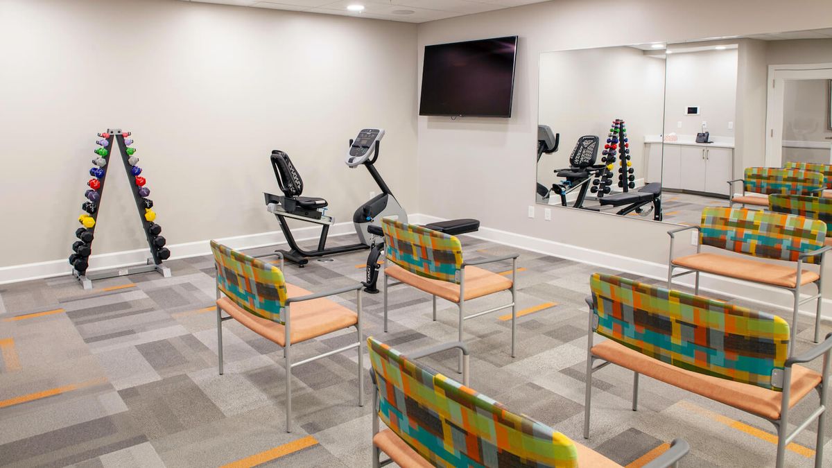 A small fitness room with exercise equipment and seating arranged in front of a wall-mounted TV.