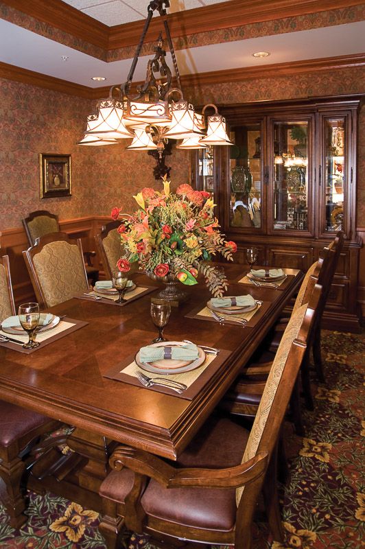 An elegantly set dining room table with a floral centerpiece and a chandelier overhead.