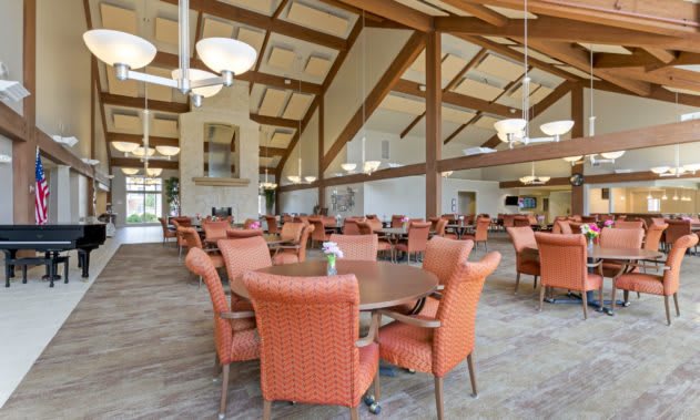 Spacious dining hall with wooden beams and orange chairs.