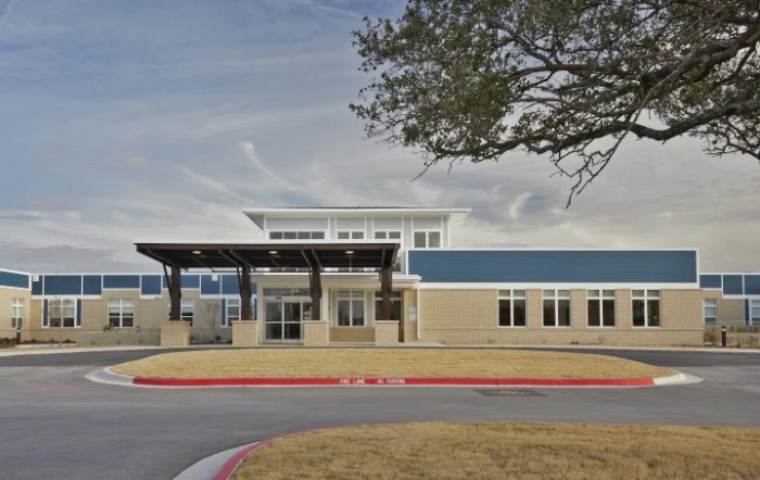 A modern school building with a blue and beige facade under a cloudy sky.