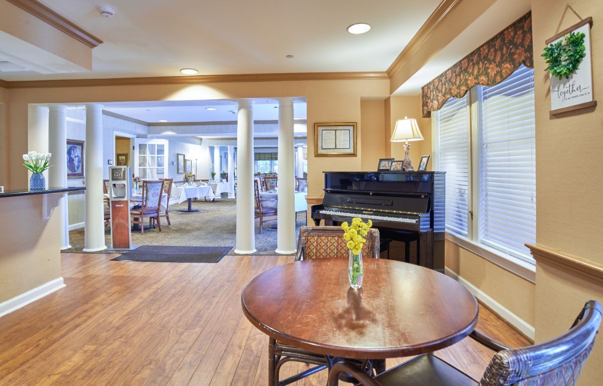 A cozy living space featuring a piano and a round table with a vase of flowers.