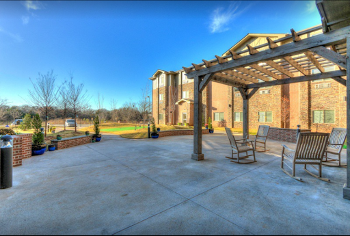 A serene outdoor patio area featuring rocking chairs under a pergola, surrounded by lush greenery and a clear blue sky.