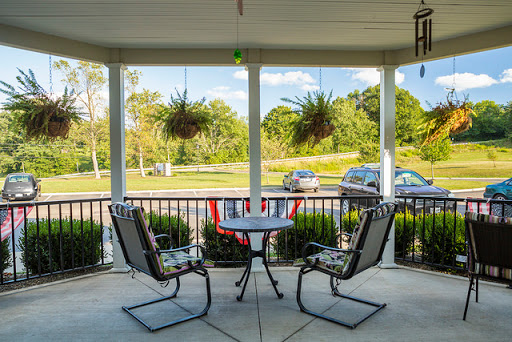A cozy outdoor porch with two chairs and a table, surrounded by greenery.