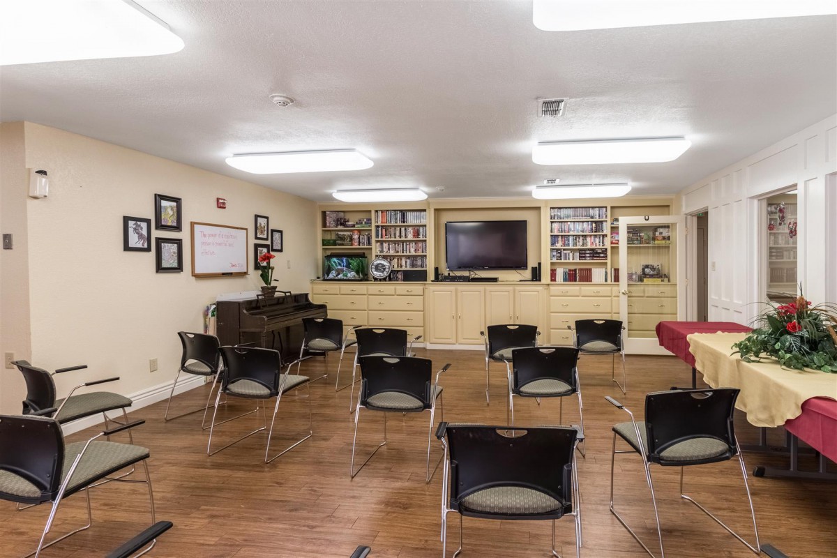 An empty classroom with chairs arranged in rows, a piano, and a television in front of bookshelves.