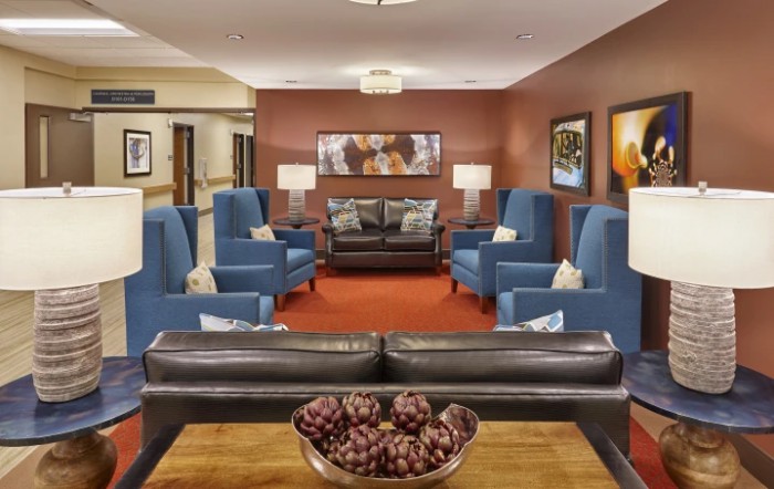 A modern lobby featuring blue armchairs and a brown sofa, with decorative artwork on the walls.