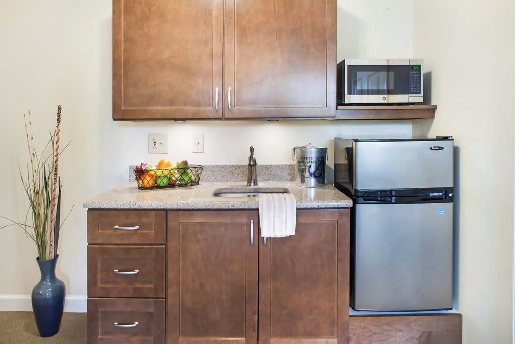 A compact kitchen space with wooden cabinets, a small refrigerator, a microwave, and a countertop with a fruit bowl.