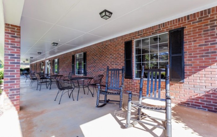 A spacious porch with rocking chairs and patio furniture along a brick wall.