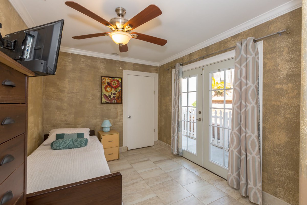 A cozy bedroom with modern decor, featuring a ceiling fan and French doors letting in natural light.