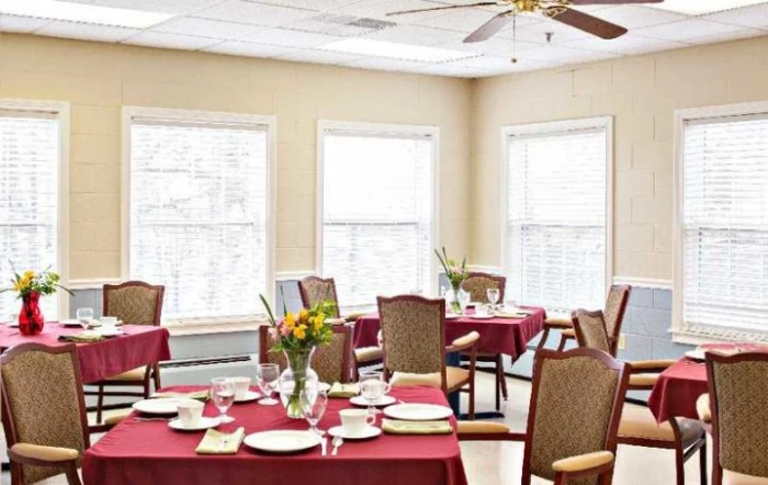 A well-lit dining room with tables set for a meal, featuring red tablecloths, elegant dishware, and floral centerpieces.