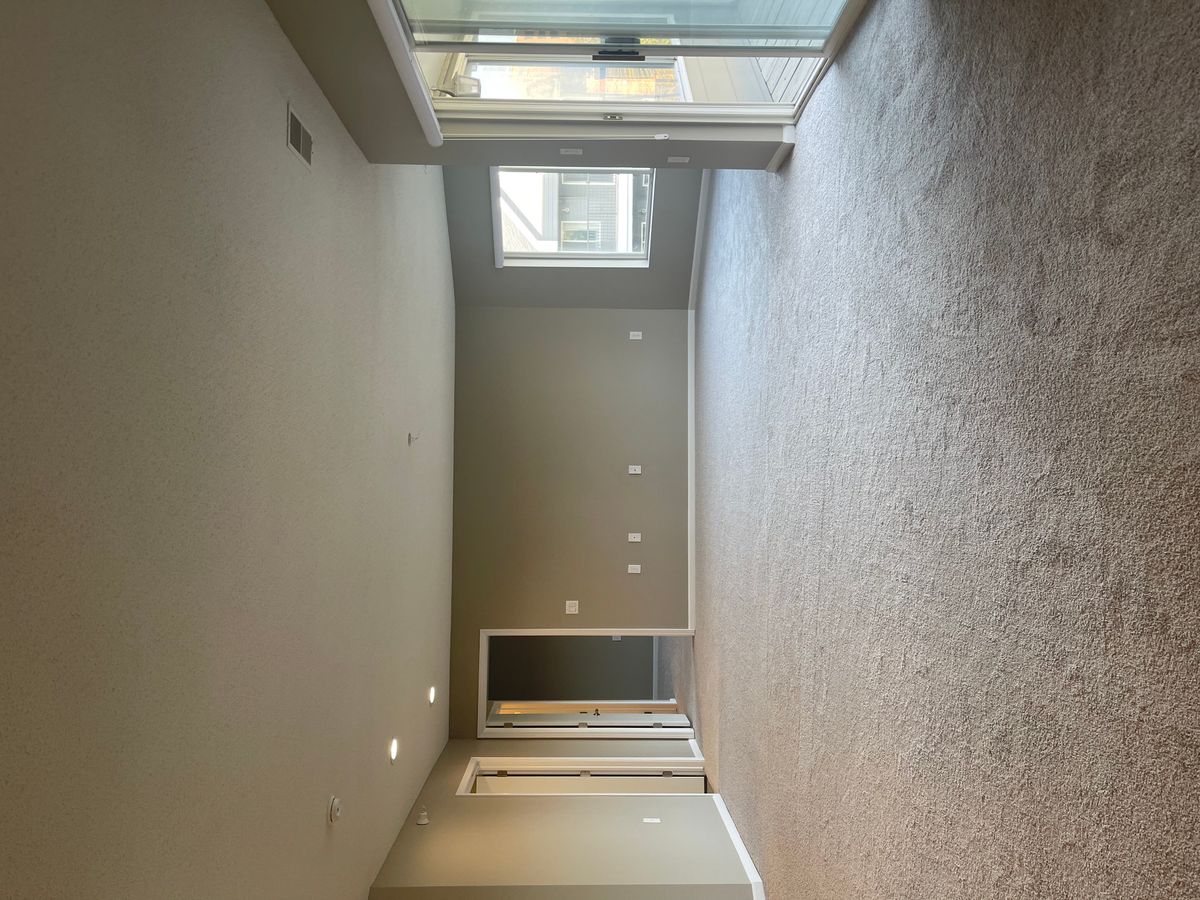 An empty room with beige carpeting, recessed lighting, and large windows offering natural light.