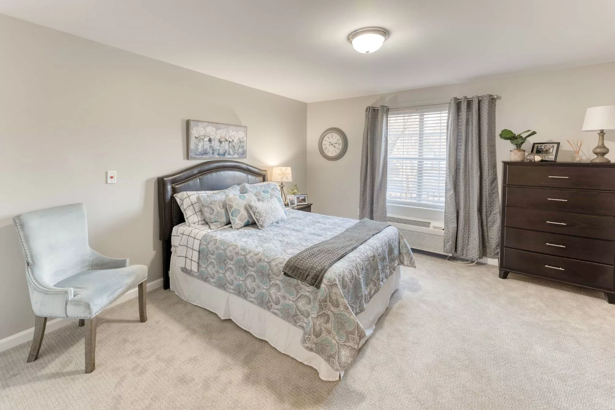 A cozy and well-decorated bedroom with a large bed, bedside table, lamp, and window with curtains.