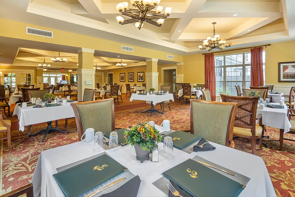 An elegant dining room with neatly arranged tables and chairs, featuring chandeliers and tasteful decor.