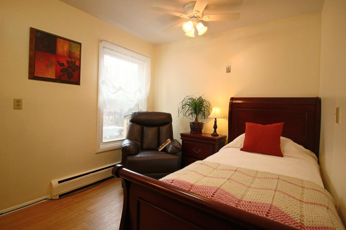 A cozy bedroom with a wooden bed frame, comfortable chair, and a warm lamp illuminating the space.