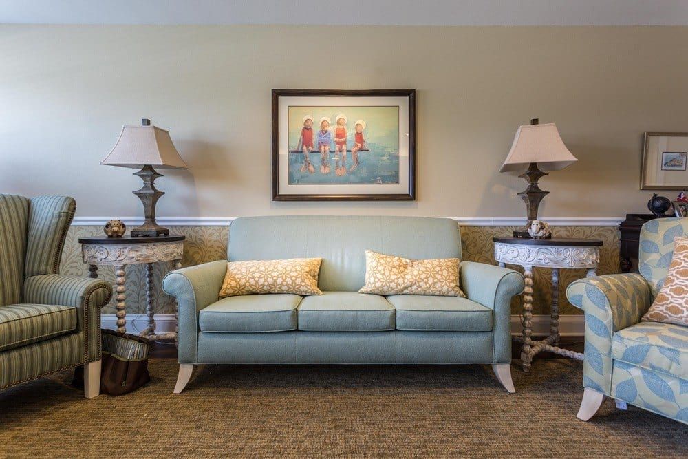 A cozy living room setup featuring a light blue sofa with decorative pillows, flanked by lamps on side tables and a vibrant painting on the wall.