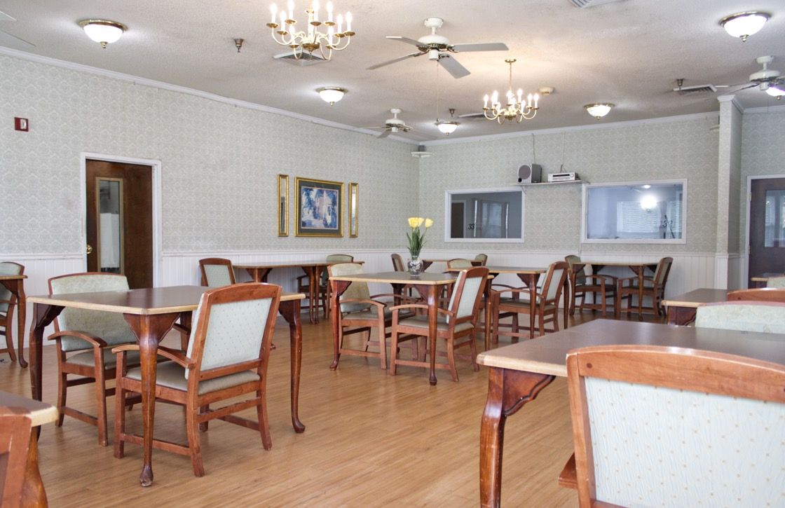 A spacious dining room with wooden tables and chairs, chandeliers, and ceiling fans.
