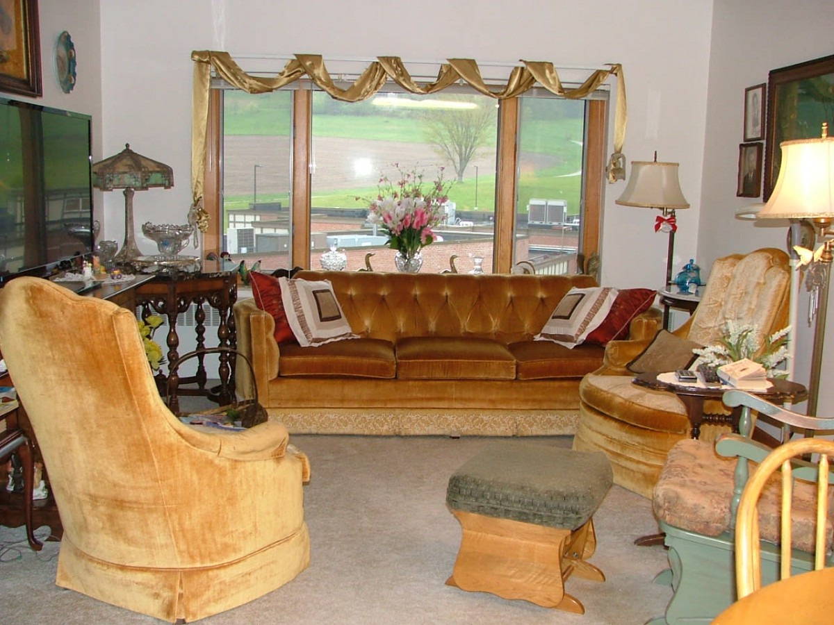 A vintage living room with a gold sofa, matching armchairs, and a decorative mirror.