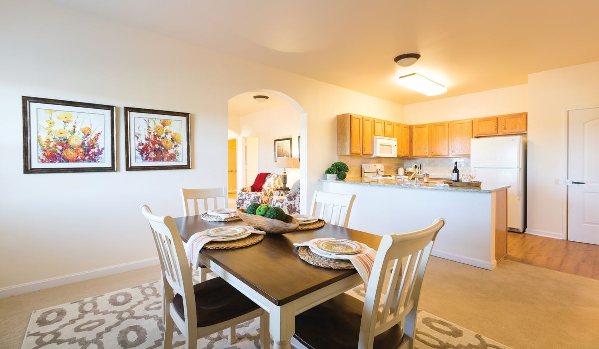 A bright and modern dining area with a view of the kitchen, featuring a dark wooden table set for four.