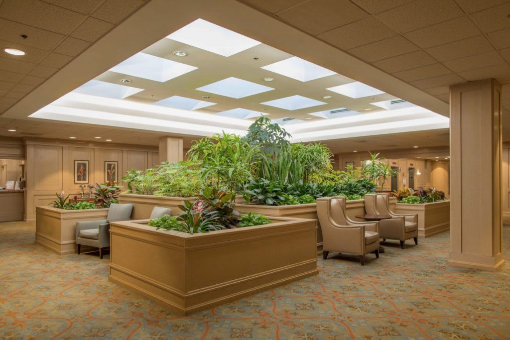 A spacious lobby area with comfortable seating and lush indoor plants under a skylight.