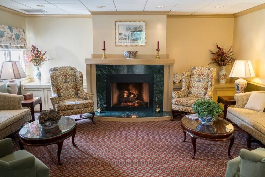A cozy living room featuring a central fireplace, flanked by two patterned armchairs and decorated with traditional elements.