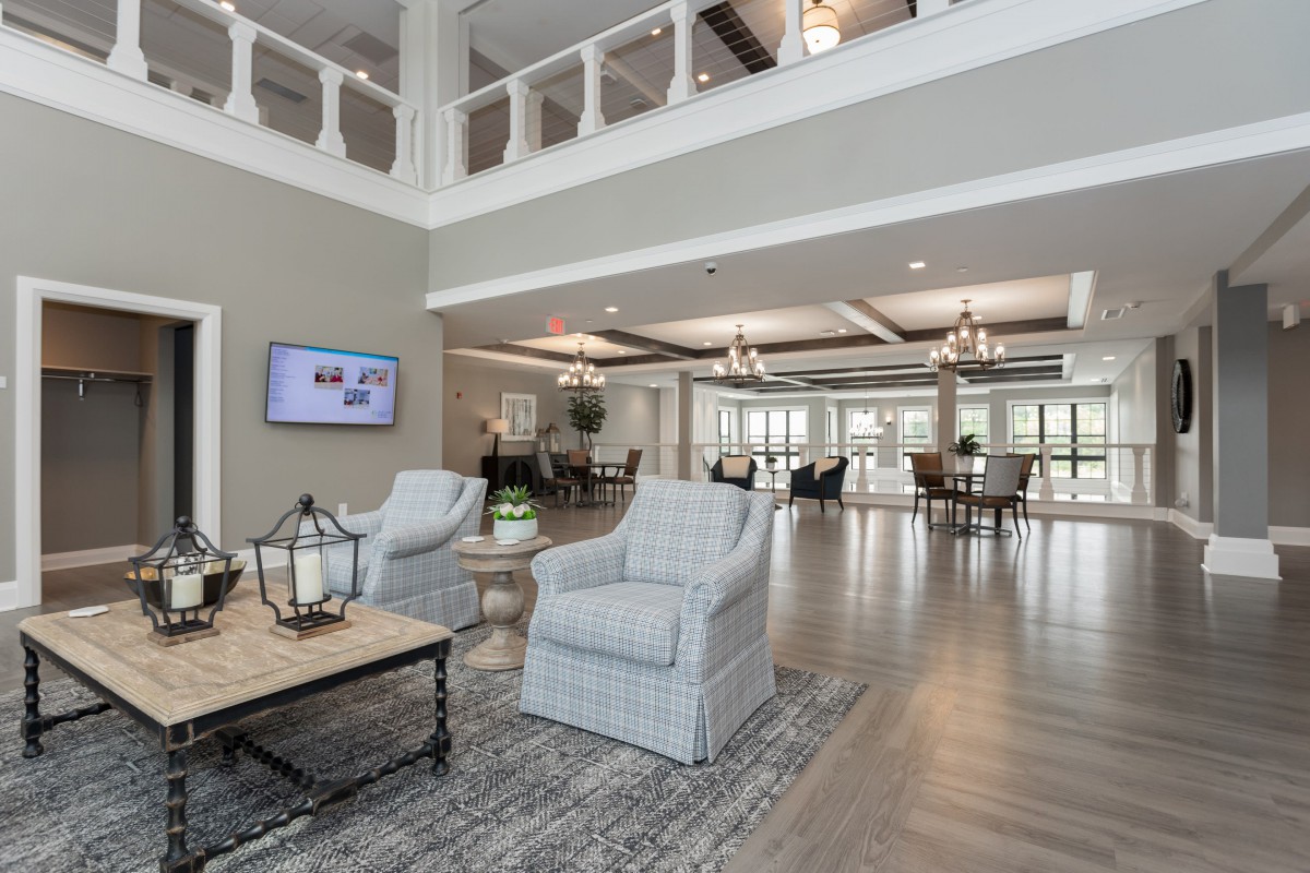 A modern and spacious living room with high ceilings, featuring comfortable chairs, a coffee table, and elegant decor, well-lit by natural light.