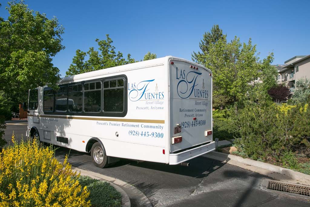 A shuttle bus parked in a lot surrounded by trees under a clear blue sky.