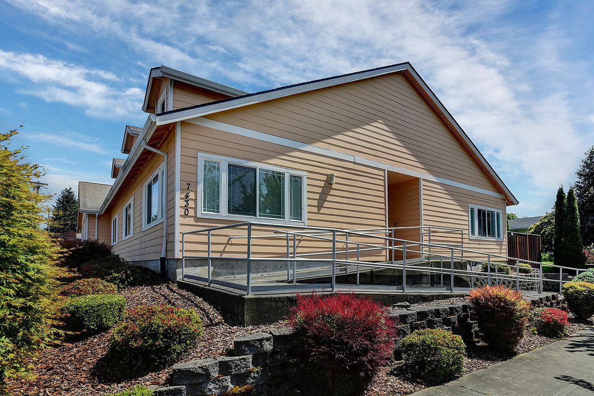 A single-story house with a wheelchair ramp and landscaped garden under a partly cloudy sky.