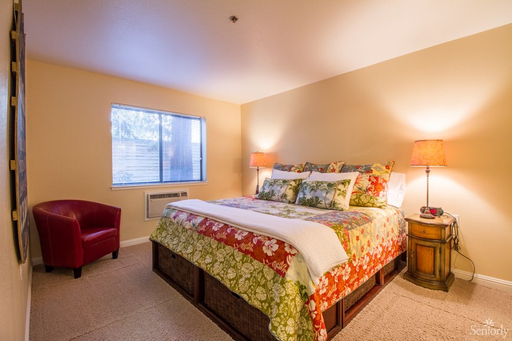 A cozy bedroom with a colorful bedspread, bedside lamps, and a window letting in natural light.