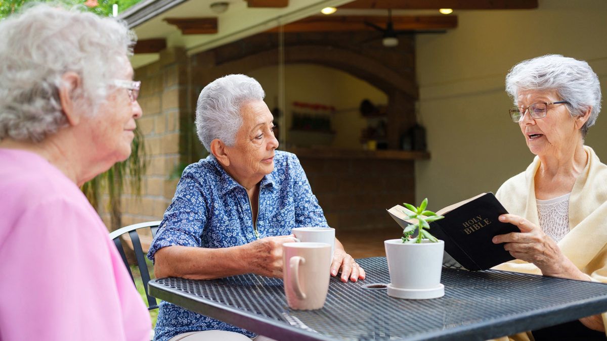 An elderly woman enjoying a conversation over coffee outside.