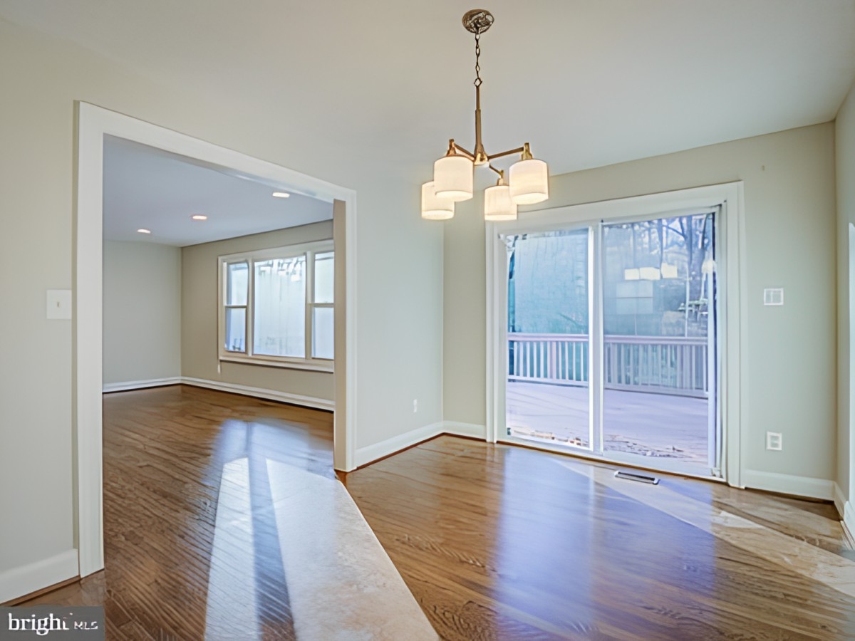 A spacious open-plan living and dining area featuring hardwood floors, a modern chandelier, and large sliding glass doors for ample natural light.