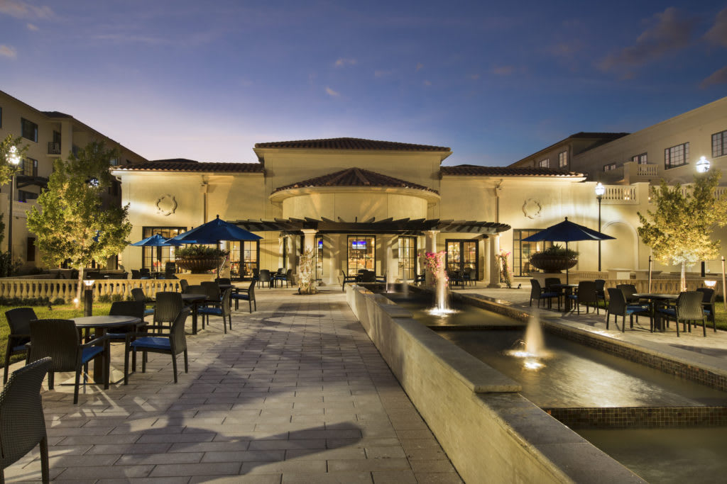 An inviting restaurant patio with outdoor seating and fountains illuminated in the evening.