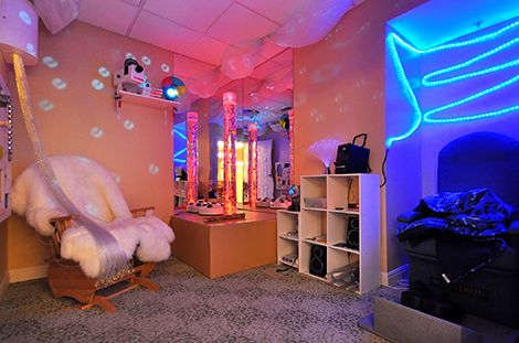 A cozy room with colorful neon lights and modern decor, featuring mirrors and shelving units.