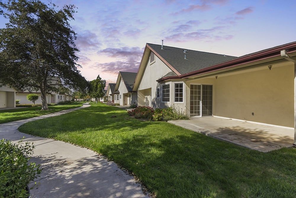 A peaceful suburban neighborhood with houses, green lawns, and a winding pathway at sunset.