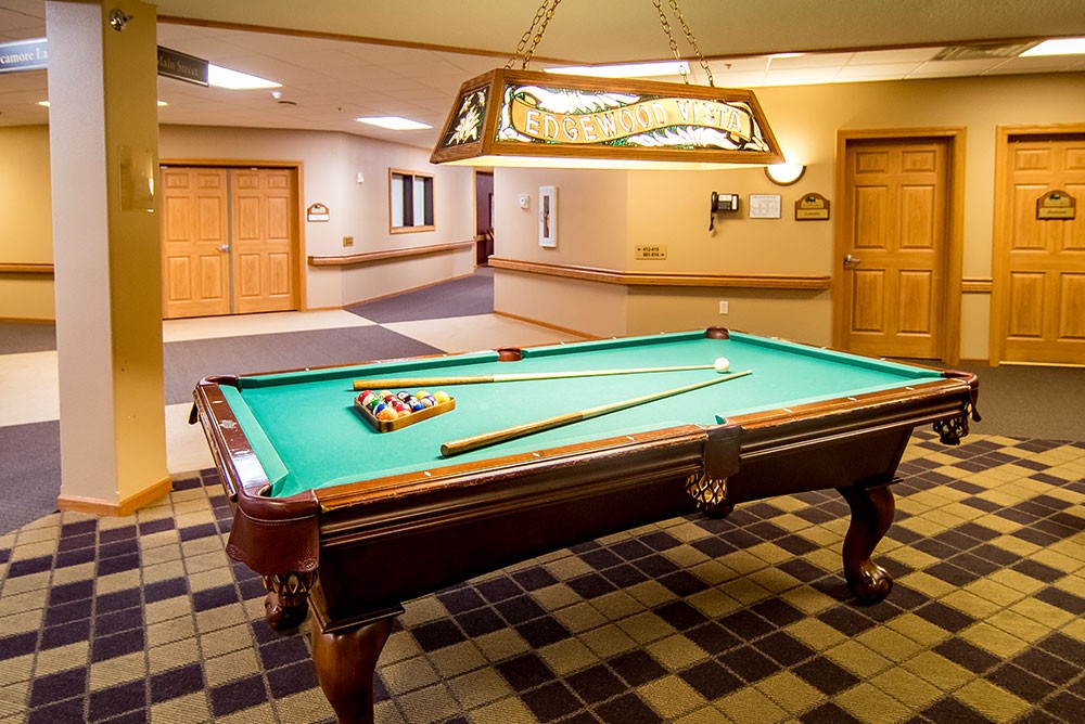 A well-lit game room featuring a pool table with cue sticks and balls ready for play.
