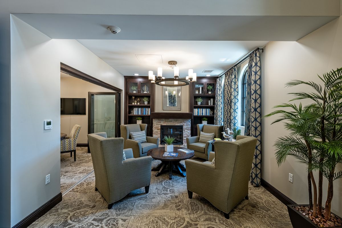 A cozy and elegant living room with armchairs surrounding a fireplace, flanked by bookshelves.
