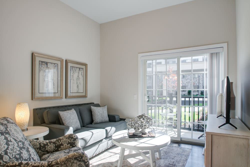 A bright living room with a cozy sofa, armchair, and coffee table, featuring large sliding glass doors that let in natural light.