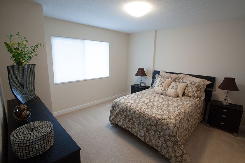 A cozy bedroom with a bed, nightstand, and a window letting in natural light.