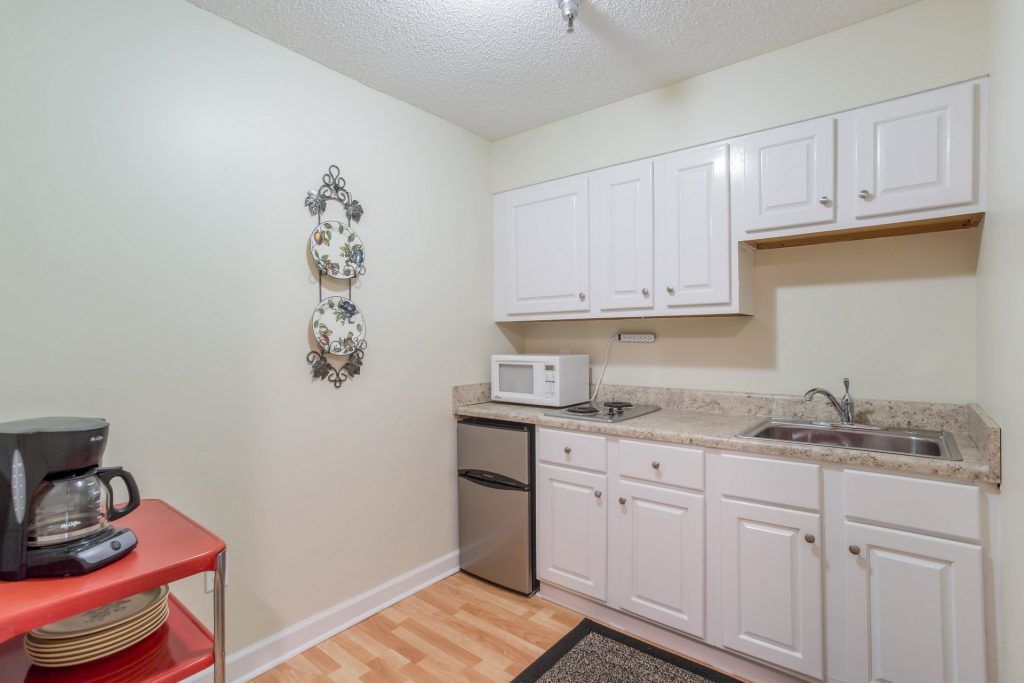 A compact kitchen featuring white cabinets, a microwave, mini fridge, and decorative plates on the wall.