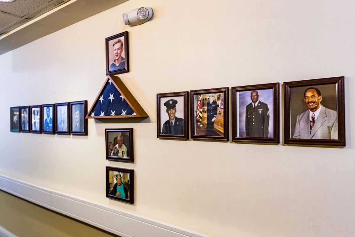 A hallway display featuring framed military photos and a folded American flag in a triangular case.