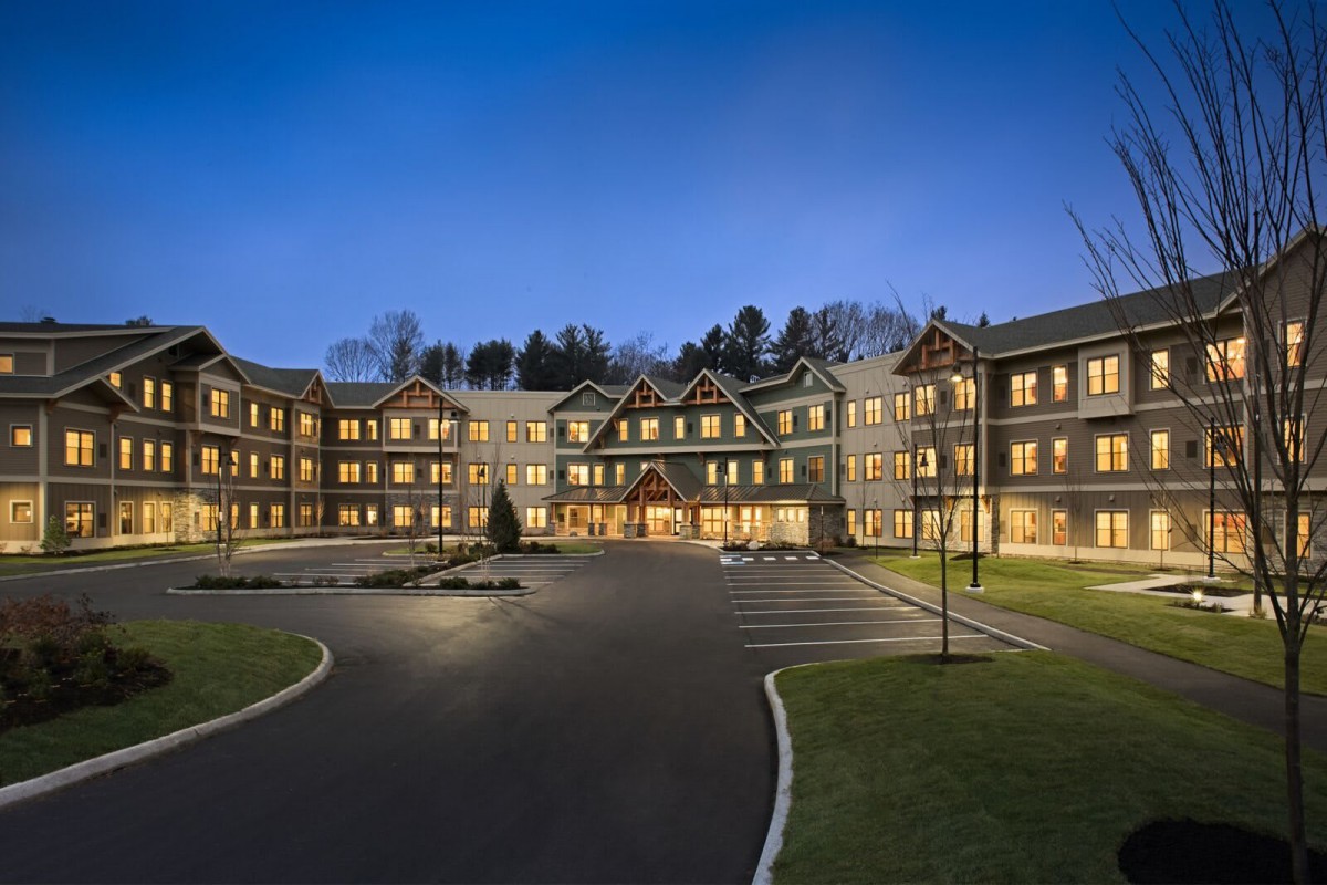 A well-lit hotel building at night with a spacious parking lot in front.