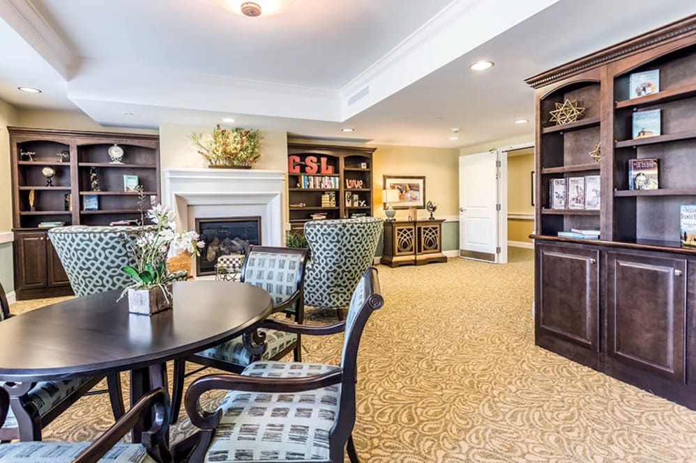 A cozy living room featuring a dining table with chairs, a fireplace, and bookshelves filled with decor items.